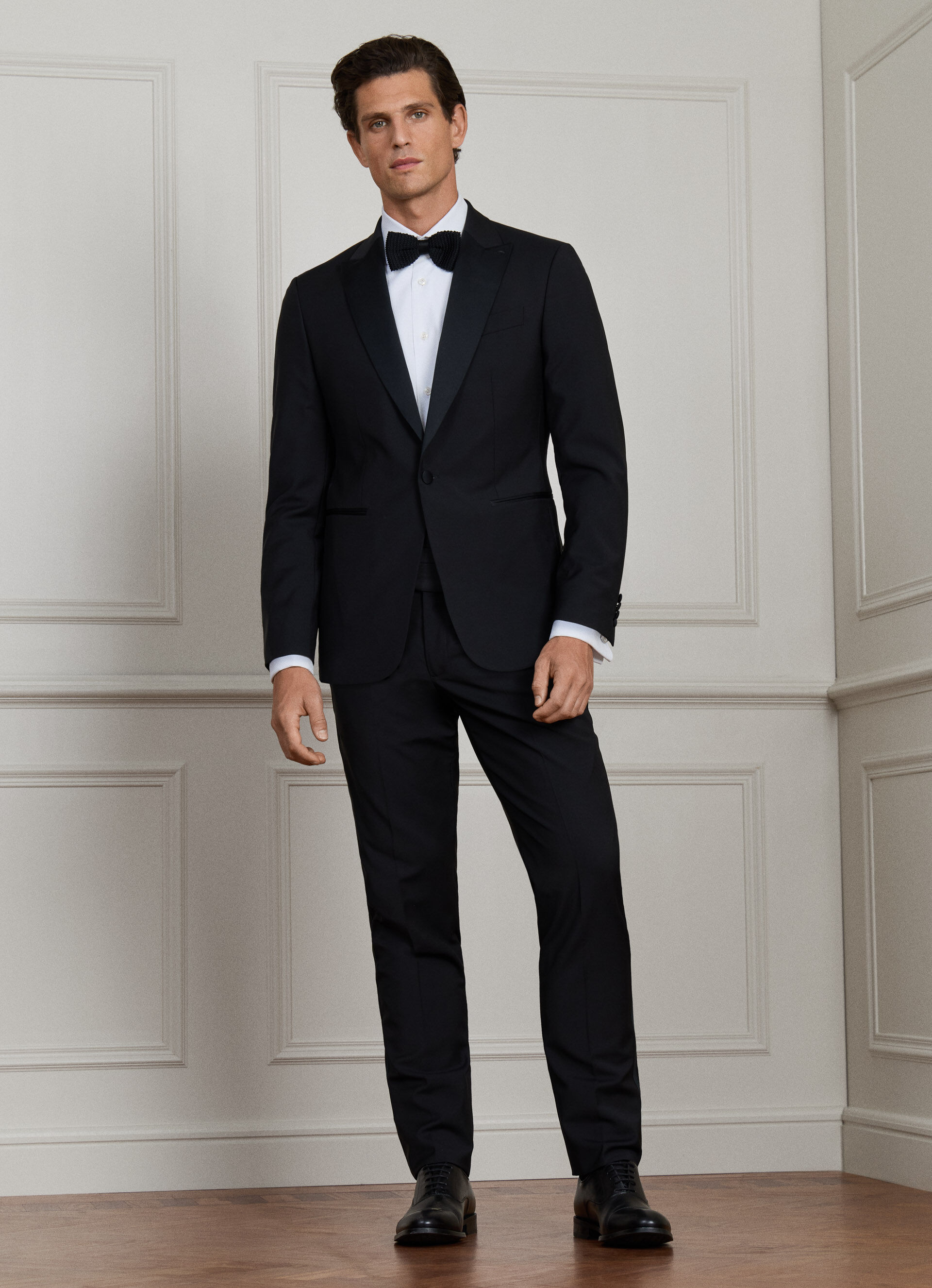 A black dinner suit with satin notch lapels and a satin trouser stripe, shown on a model.